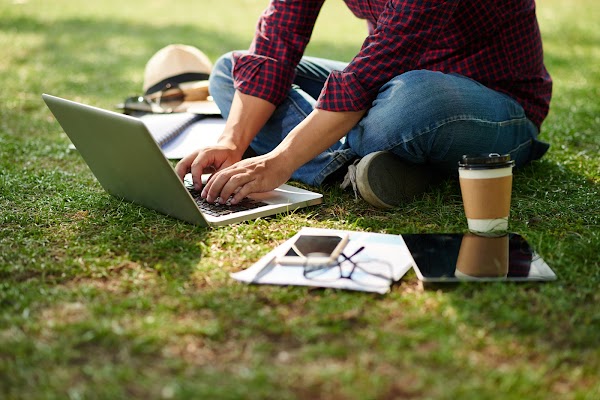 Cropped image of student sitting on the ground and working on laptop