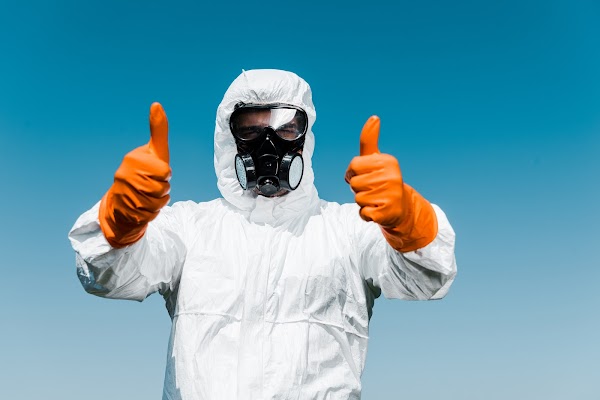 exterminator in protective mask and uniform standing and showing thumbs up