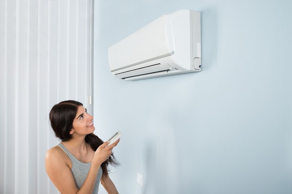 39653653 – young happy woman holding remote control air conditioner in house