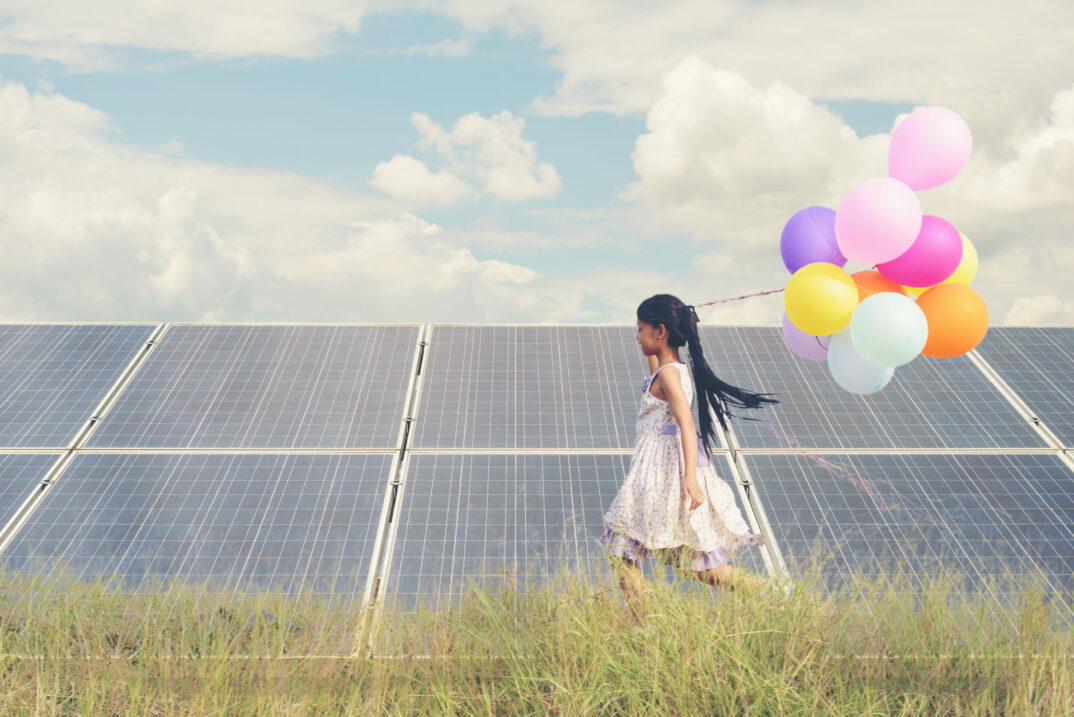 A funny girl carrying a colorful balloon running in a meadow wit